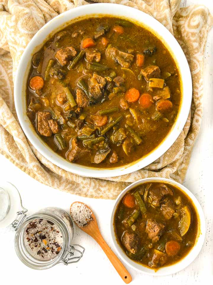 large and small white bowls with slow cooker beef stew and a jar of season salt and wooden spoon