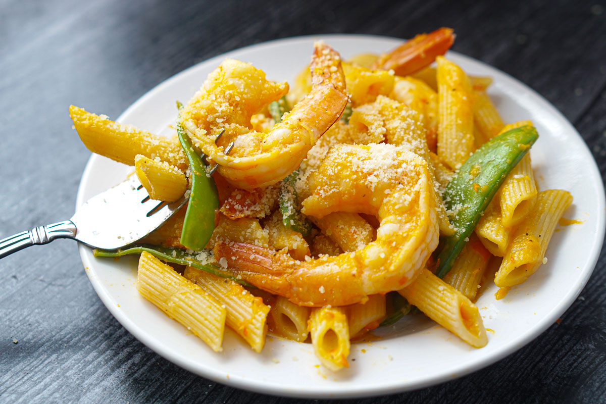 a plate of red pepper shrimp pasta with a fork and grated cheese