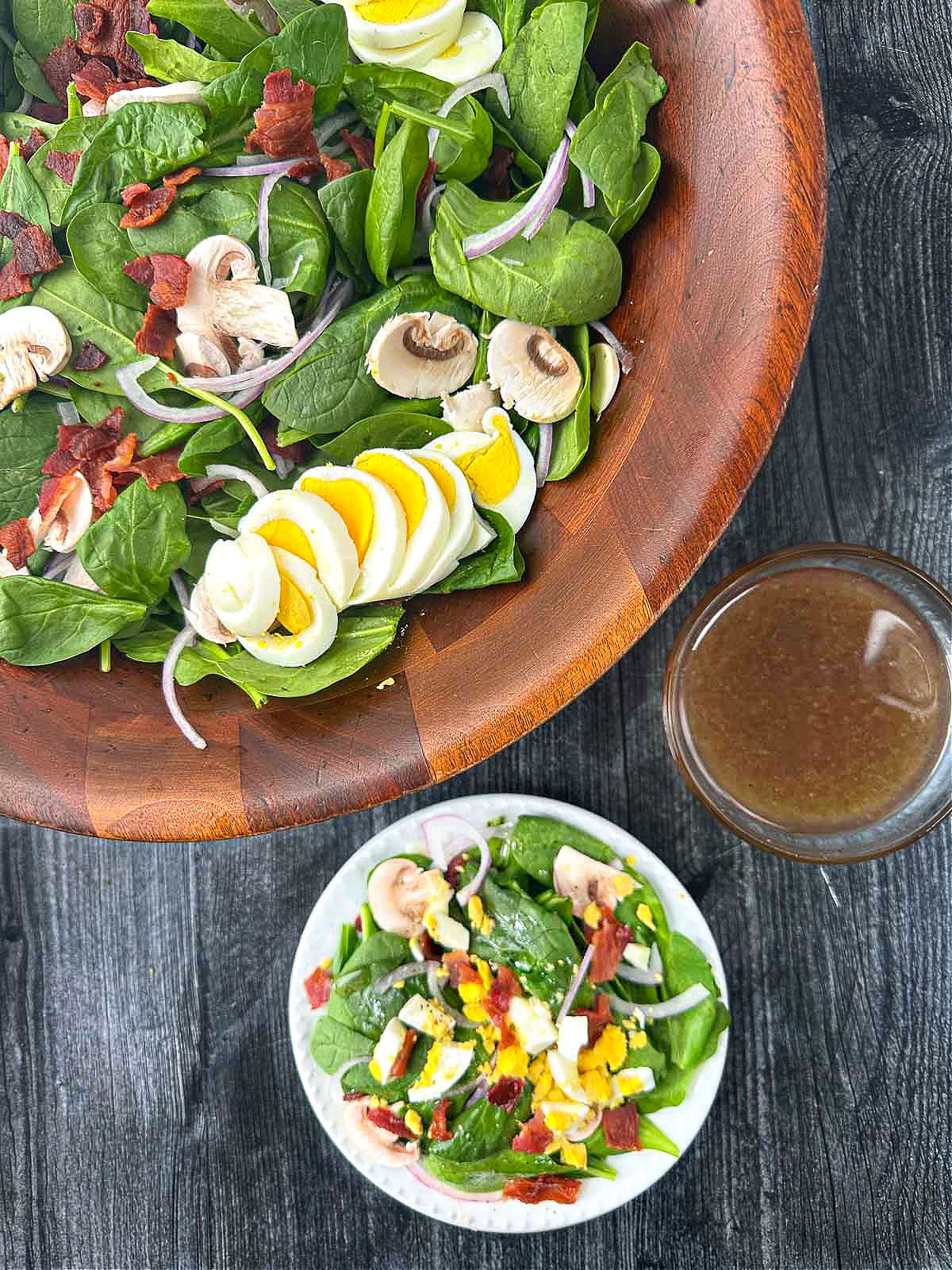 aerial view of wooden bowl and plate with spinach salad and bowl of bacon dressing