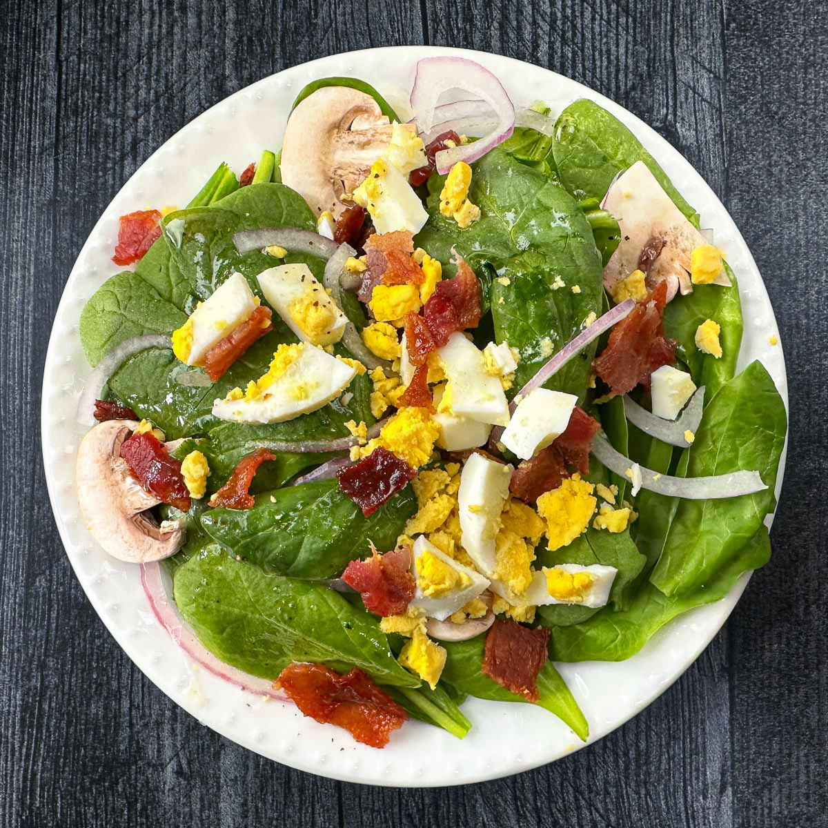 white plate with spinach salad with bacon dressing