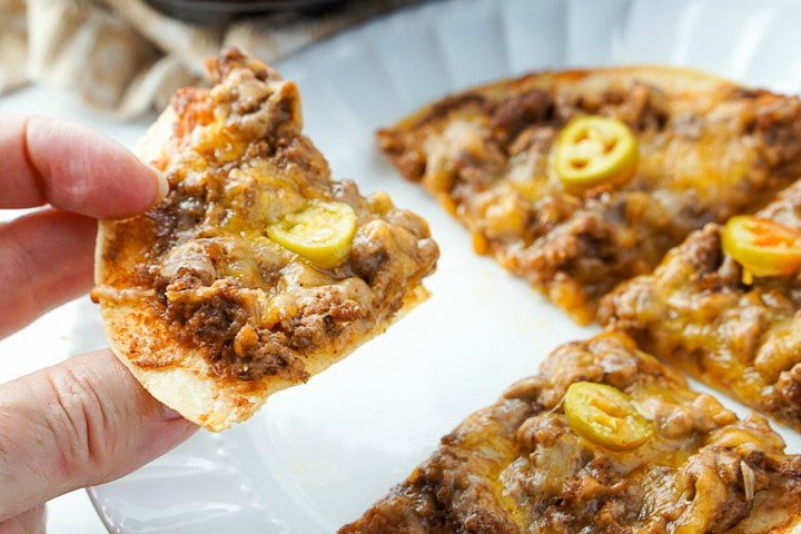 fingers holding one of the nachos from a plate of 4