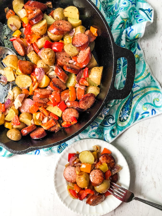 cast iron skillet with kielbasa recipe for dinner on a blue tea towel and white plateful 