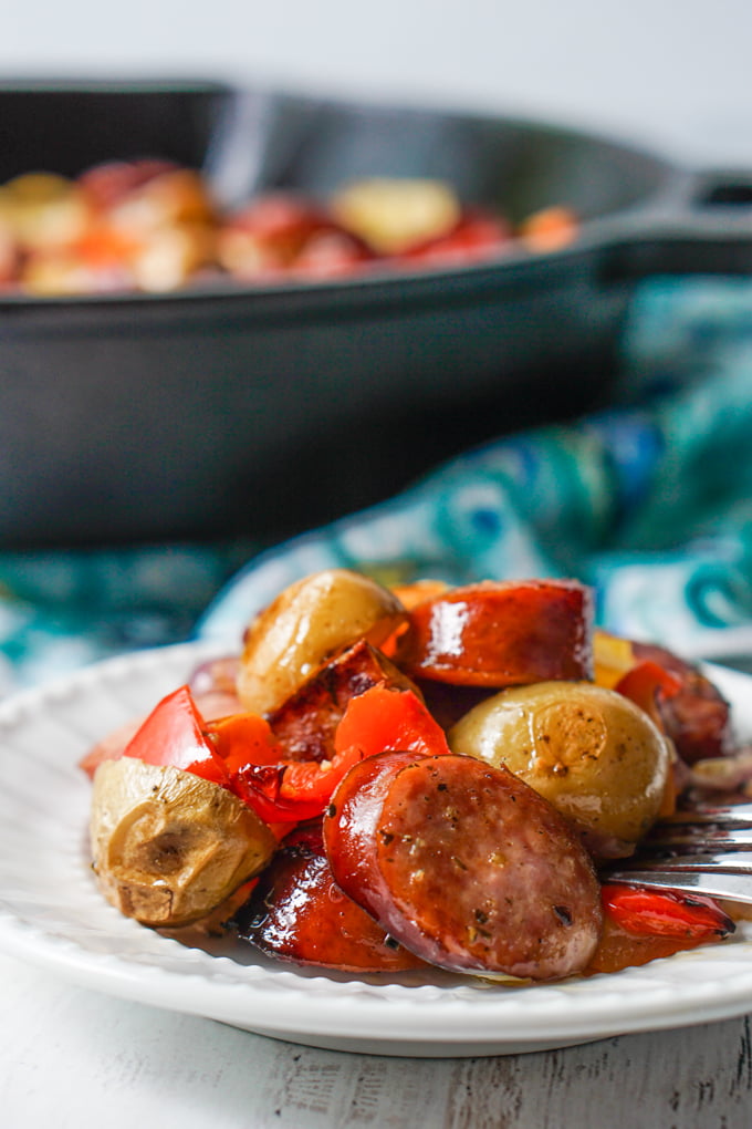 closeup of a white plate with the potatoes, peppers and kielbasa with a cast iron skillet in background