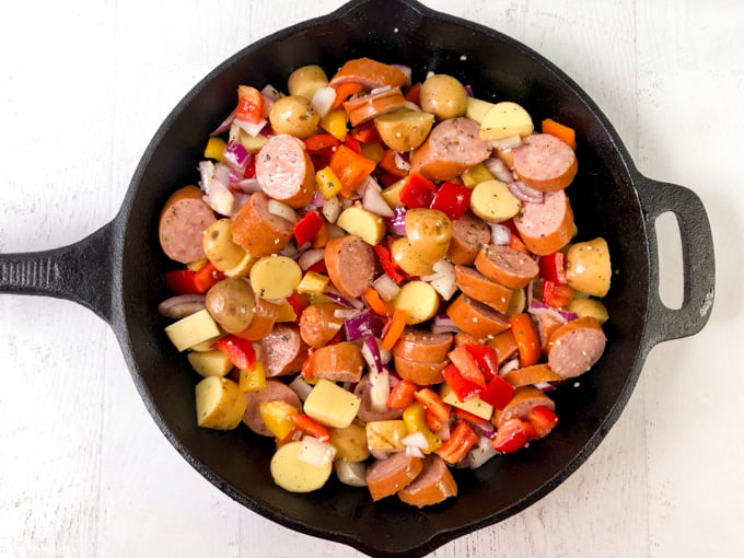 cast iron skillet with raw potatoes, peppers and kielbasa