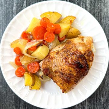 white plate with roasted chicken thighs and potatoes and veggies