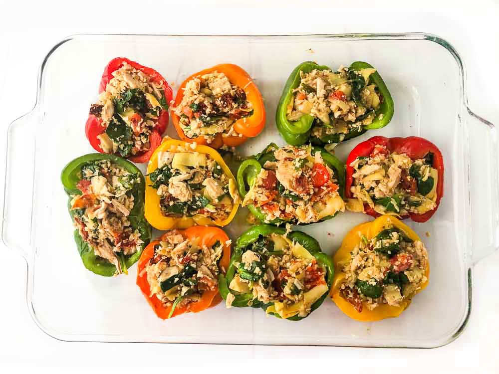 glass baking dish with 10 cooked stuffed peppers with chicken, artichokes, sun-dried tomatoes and spinach