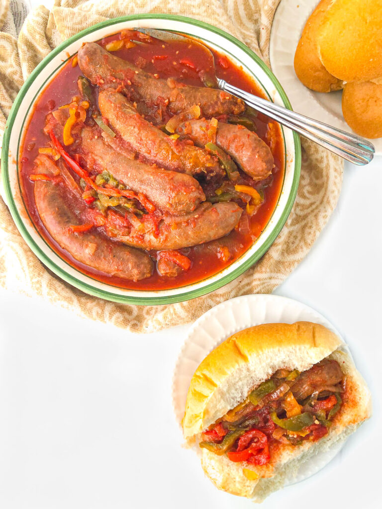 aerial view of a bowl of hot sausage and peppers and a sausage sub sandwich on a white plate