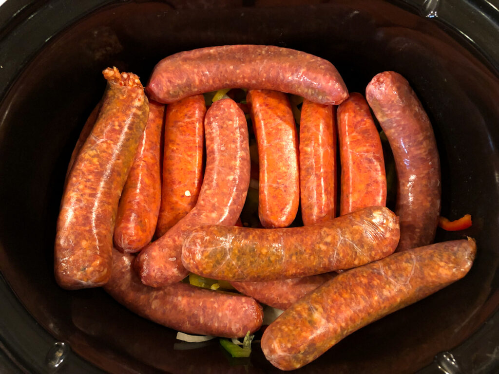 crock with raw Italian sausages on top of veggies