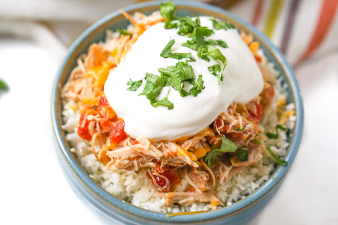 blue bowl with cauliflower rice and slow cooker salsa chicken topped with sour cream and cilantro