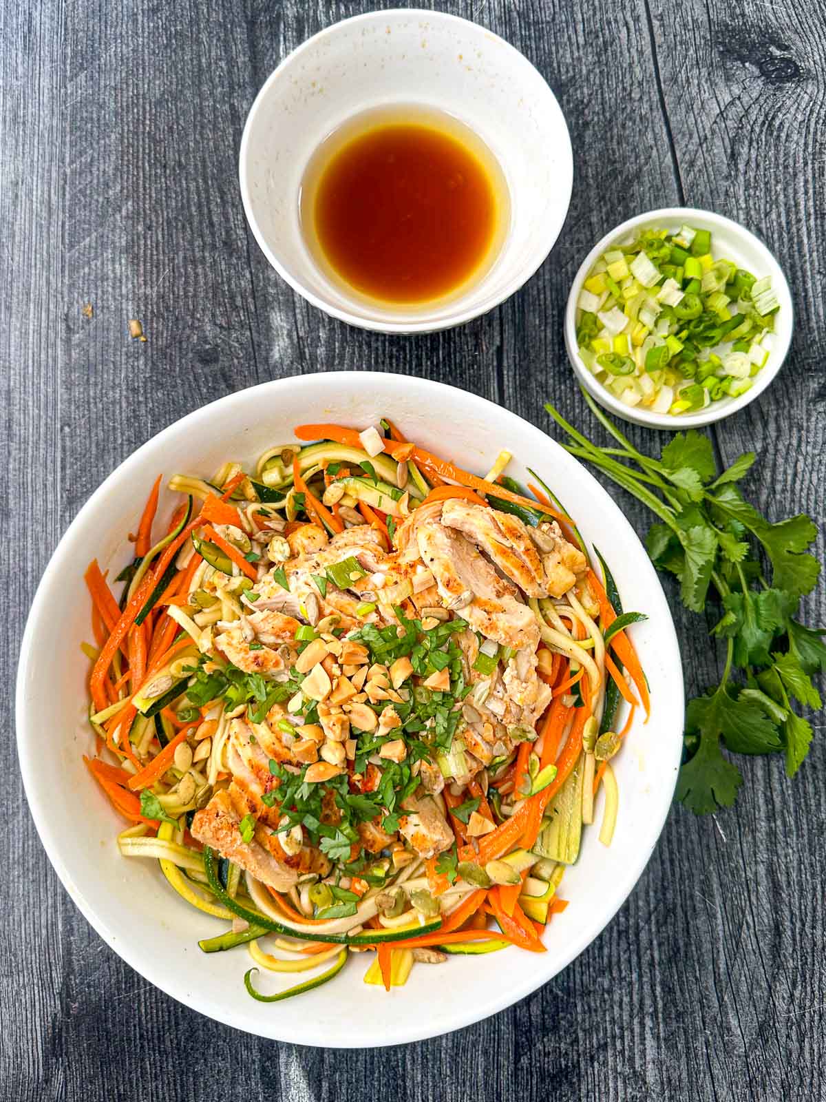 aerial view of a big bowl of Asian noodles salad with fresh cilantro and a bowl of dressing