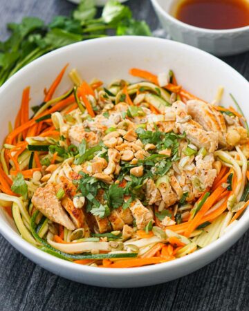 white bowl with Asian zucchini noodle salad topped with chicken