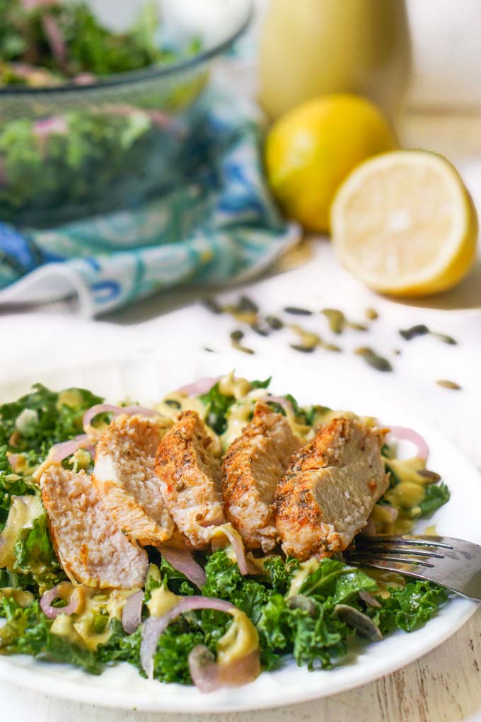 plate of kale salad with chicken breast with dressing and lemons in the background