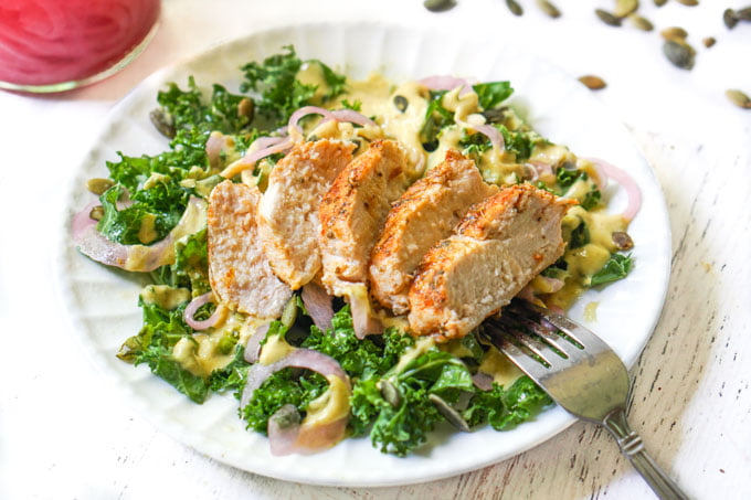 white plate with kale salad and a chicken breast on top