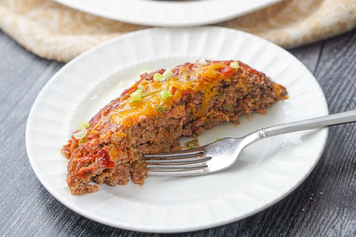 closeup of a slice of taco meatloaf with a fork on a white plate