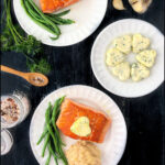 white plate with seared salmon and an herb butter pat on top and text