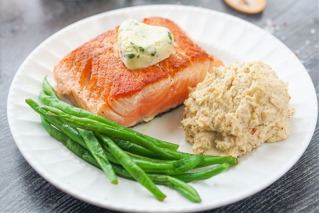 finished seared salmon with a pat of lemon herb butter and mashed cauliflower and green beans
