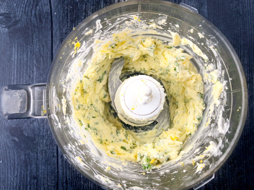 food processor bowl with softened butter mixture with parsley, garlic and lemon zest