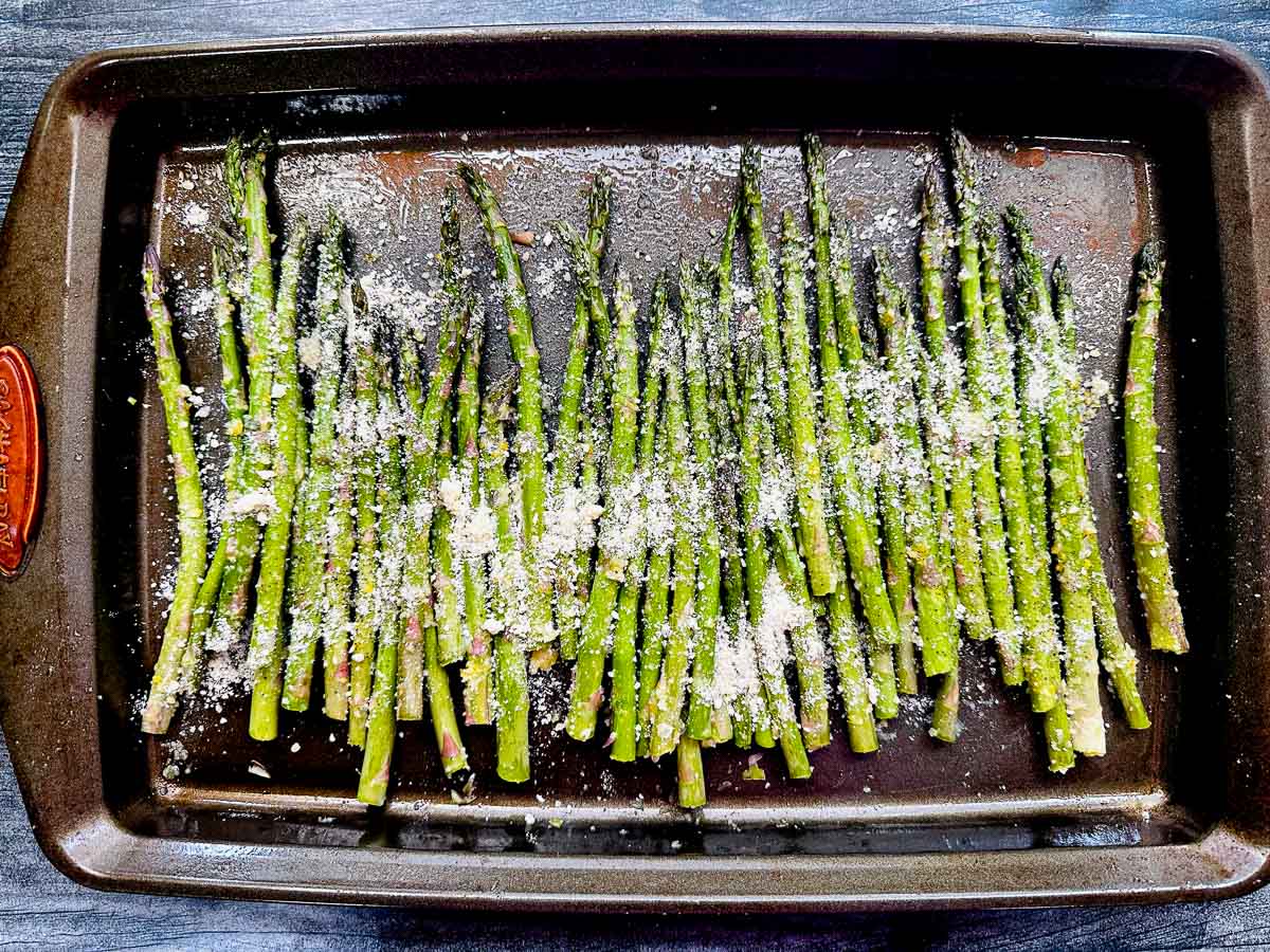 baking try with raw asparagus spears with sprinkled grated cheese on top