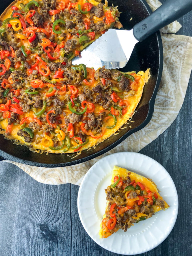 aerial view of a skillet and white plate with low carb breakfast pizza and a silver spatula