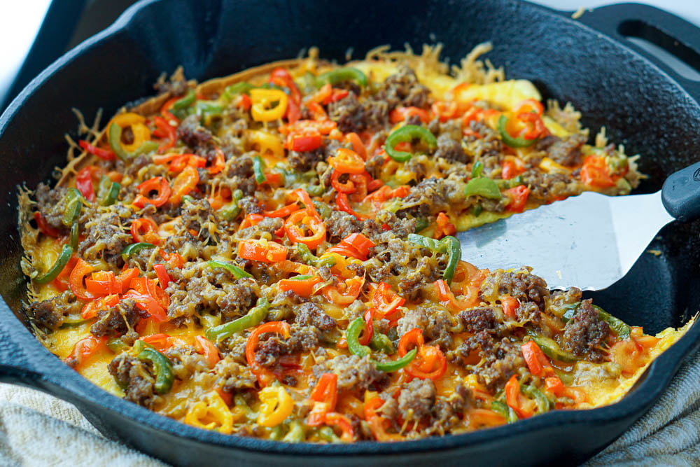 closeup of a cast iron skillet with a spatula and piece of egg pizza missing.