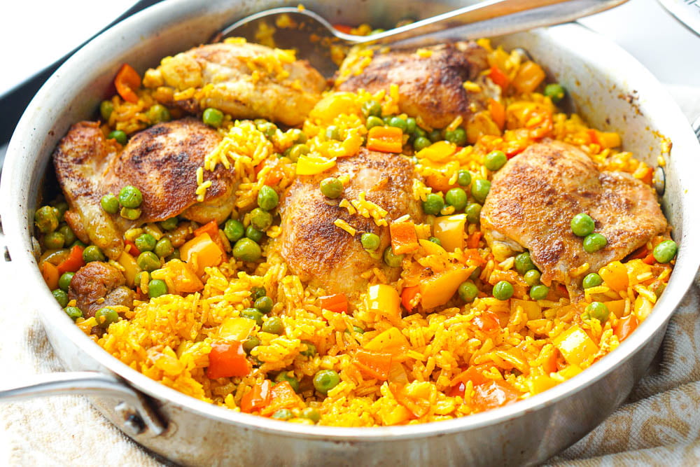 a silver pan with chicken thighs and yellow rice with peppers and peas 