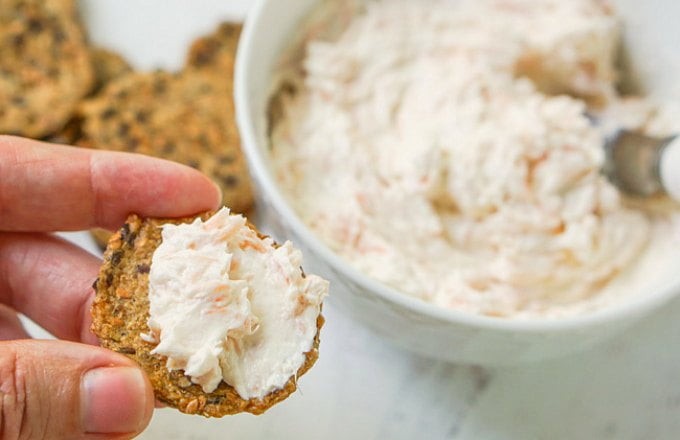 hand holding cracker with salmon dip and a bowl of low carb smoked salmon dip