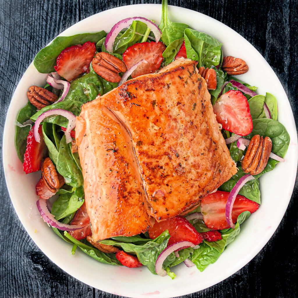 white bowl with spinach and strawberry salad and a piece of salmon on top