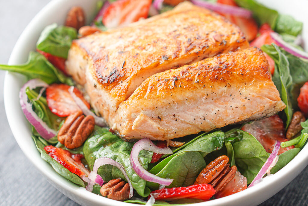 closeup of white bowl with salmon on spinach strawberry salad