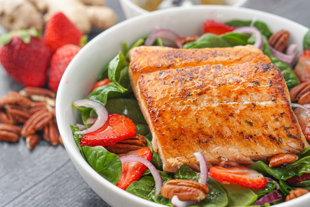 closeup of white bowl with salmon on spinach strawberry salad
