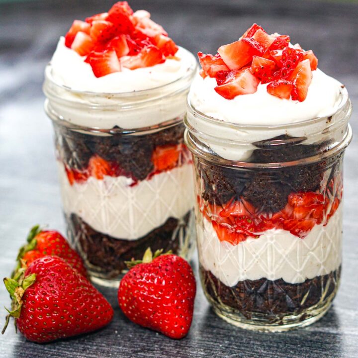 Closeup of 2 keto cheesecake parfaits with fresh strawberries and chocolate cake layers.