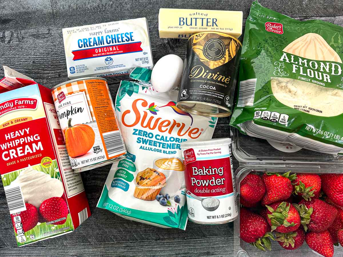Recipe ingredients - heavy cream, pumpkin puree, cream cheese, butter, egg, cocoa powder, baking powder, sweetener, almond flour and fresh strawberries.