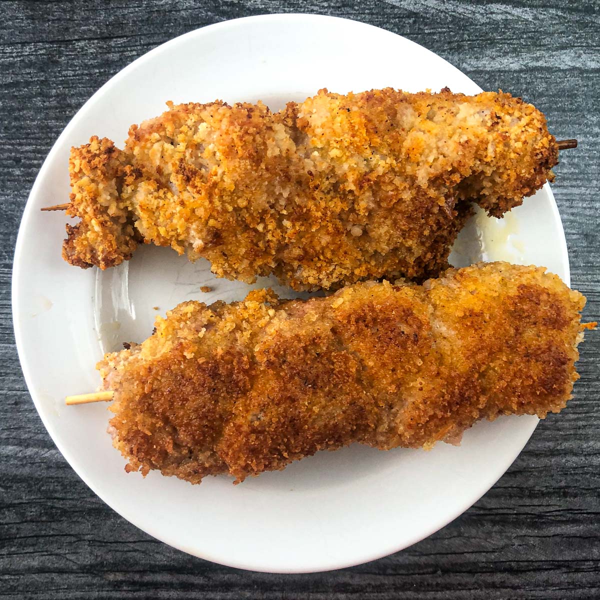 white plate with 2 pieces of chicken from the city on skewers