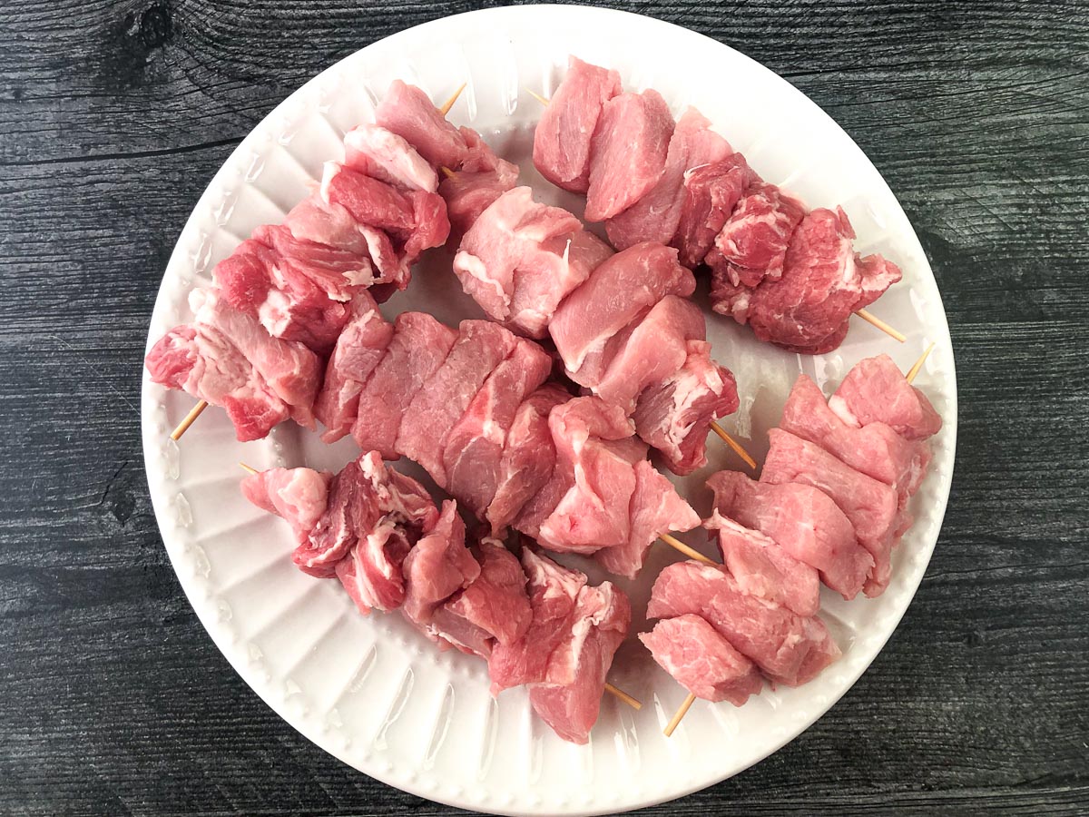 white plate with skewered pieces of raw pork ready to be breaded