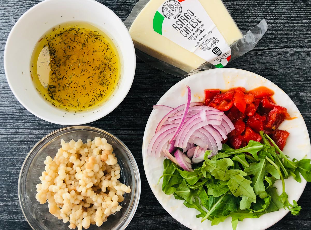recipe ingredients - dressing, israeli couscous, arugula, roasted peppers, red onions, asiago cheese