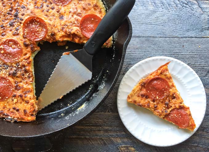 cast iron skillet with a pepperoni pizza and spatula and white plate with a slice.