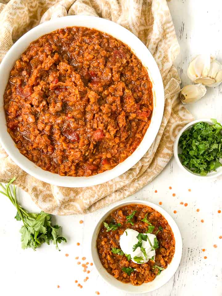 large and small white bowl with spicy Mexican red lentils chili and a bowl of and sprig of fresh cilantro