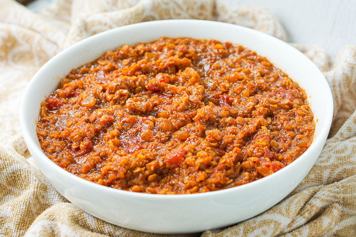 big white bowl with spicy red lentils dish and beige tea towel underneath 