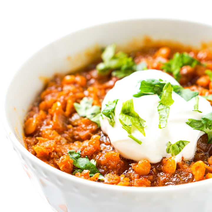 closeup of white bowl of spicy Mexican red lentils with sour cream