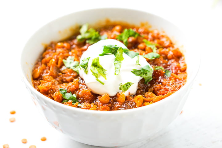 closeup of a white bowl with spicy Mexican red lentils topped with sour cream and fresh cilantro