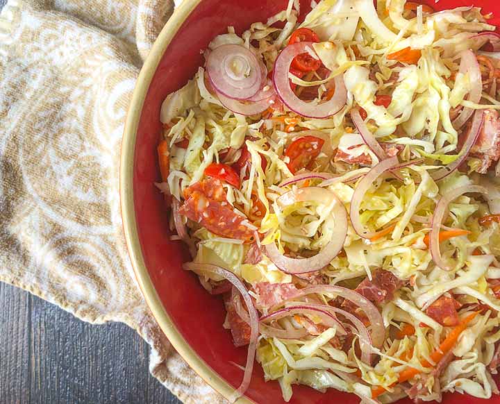 red bowl filled with antipasto keto cabbage salad with a beige tea towel 