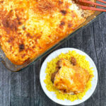 Aerial view of a pan of mom's moussaka recipe and a plate with rice and serving on top.