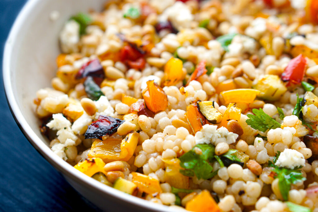 closeup of Israeli couscous side dish with vegetables, feta and pine nuts