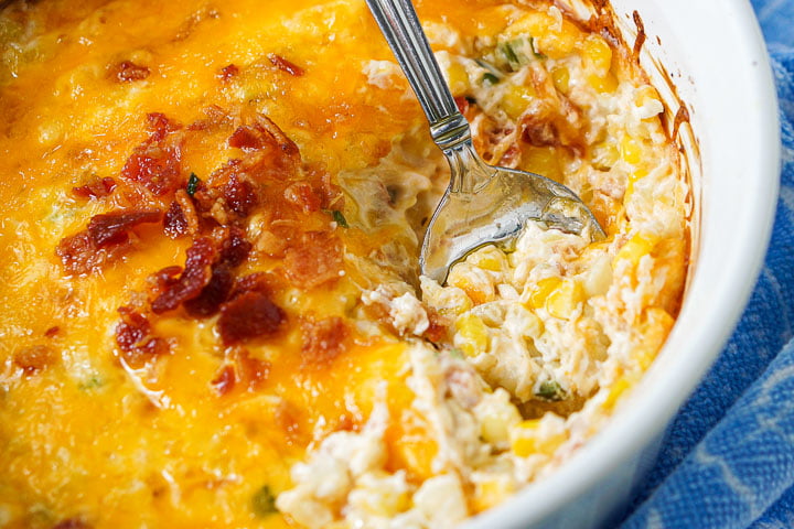 closeup of  the creamy, cheese corn dip with crumbled bacon on top and a spoon