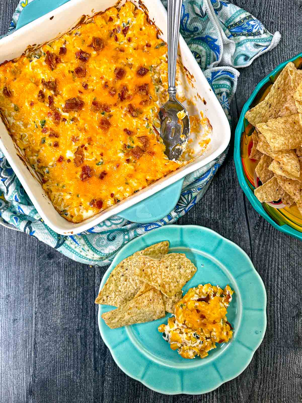 Aerial view of a baking dish with the creamy hot corn dip with a plate of tortilla chips.