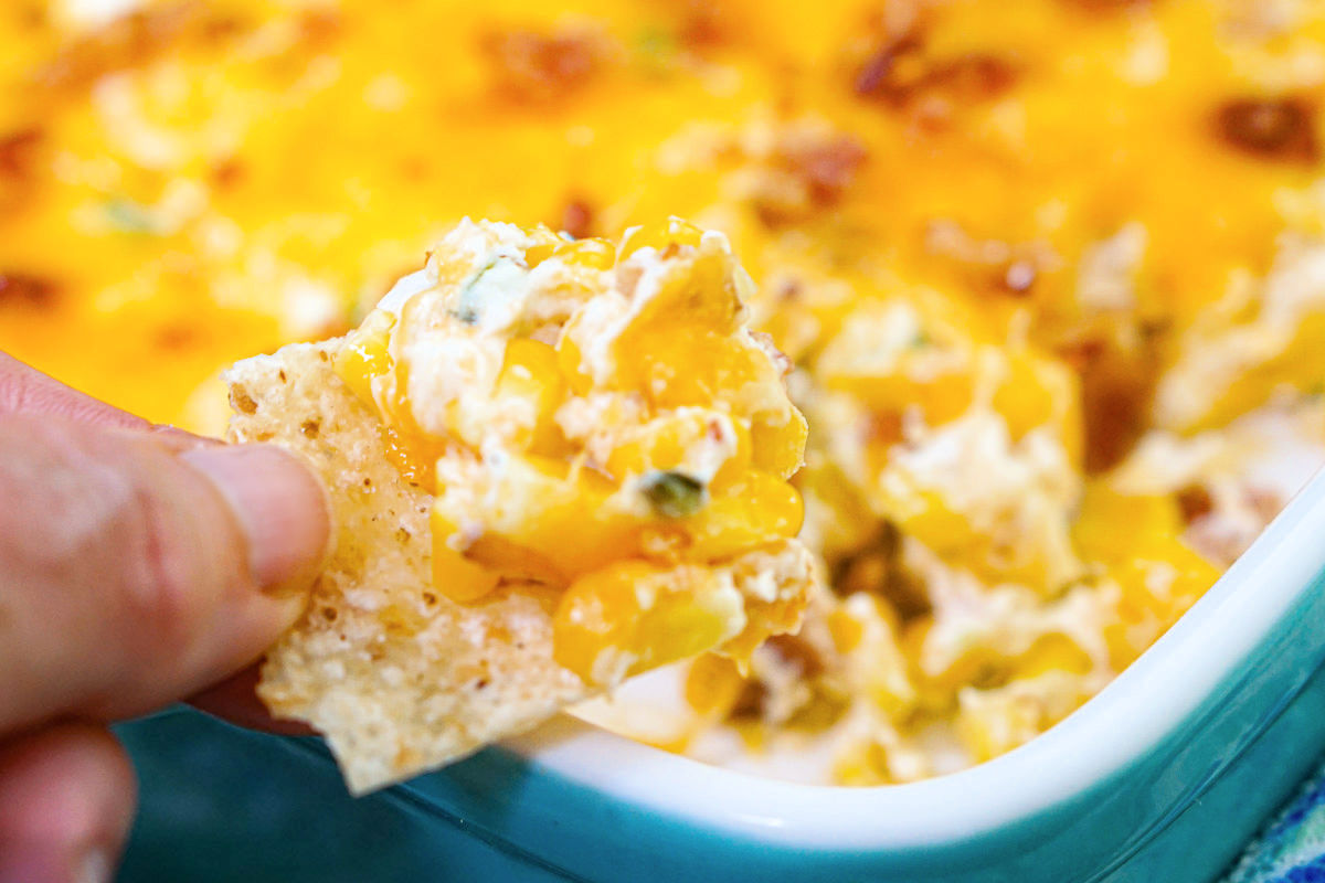 Fingers holding a tortilla chip with some of the finished recipe on top.