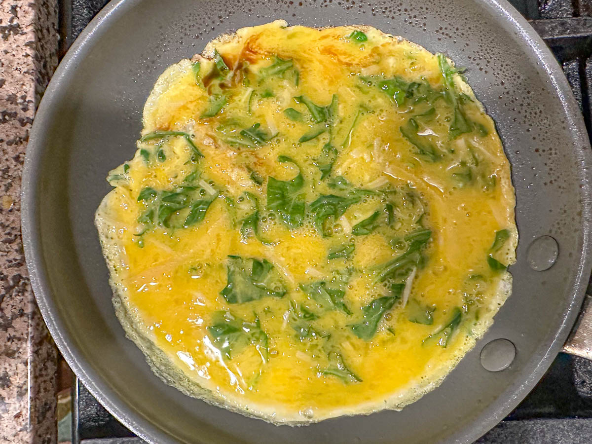 pan with raw eggs and greens