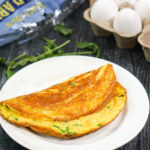 aerial view of arugula omelet on white plate with carton of eggs and a bag of arugula leavesaerial view of arugula omelet on white plate with carton of eggs and a bag of arugula leaves with text