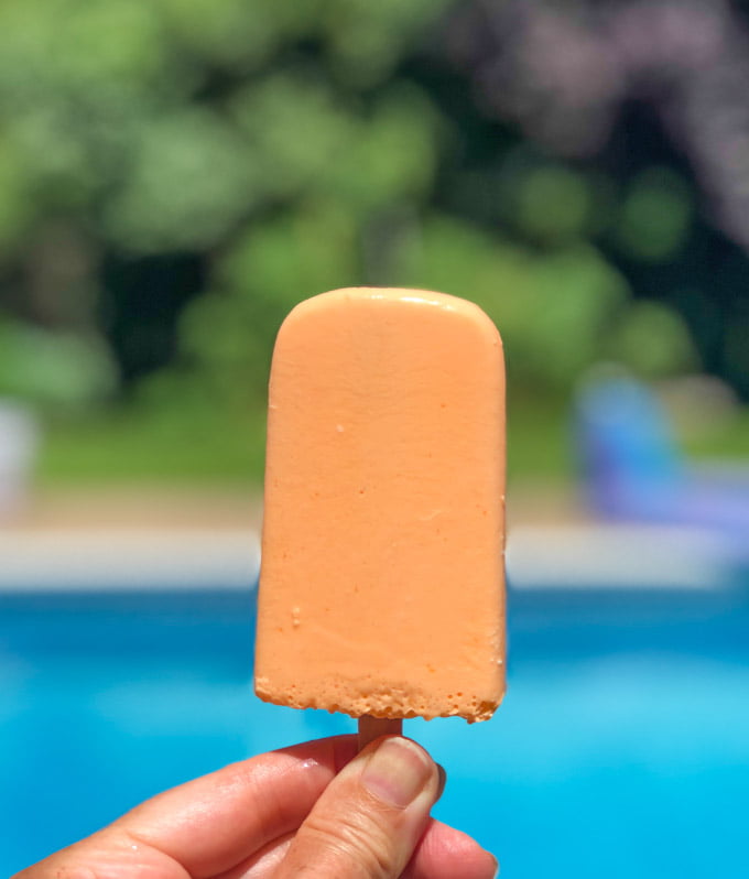 orange low carb jello pop held by hand by the pool