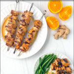 aerial view of keto grilled pork kebabs on white plate and fresh oranges and ginger with text