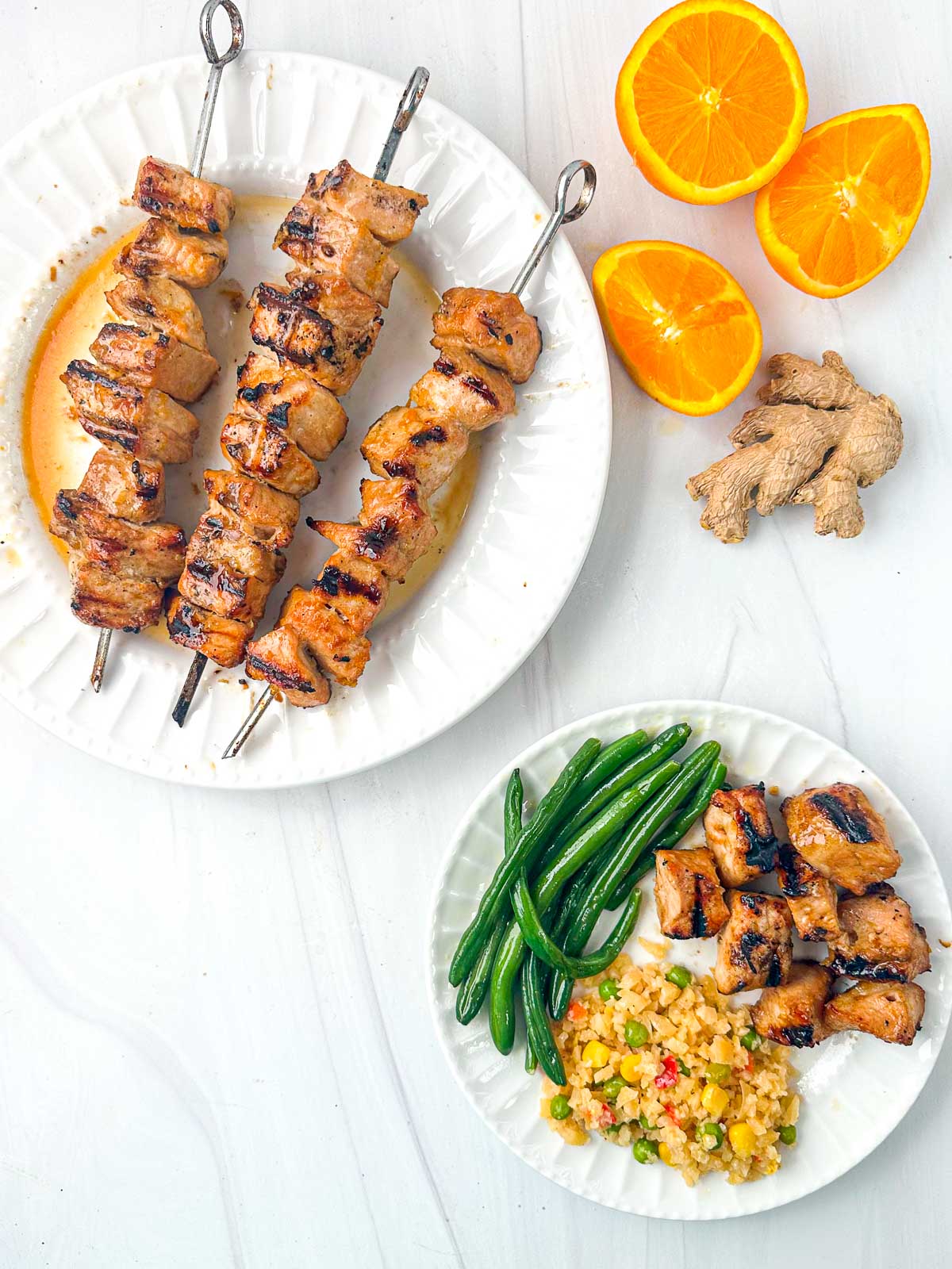 aerial view of keto grilled pork kebabs on white plate and fresh oranges and ginger
